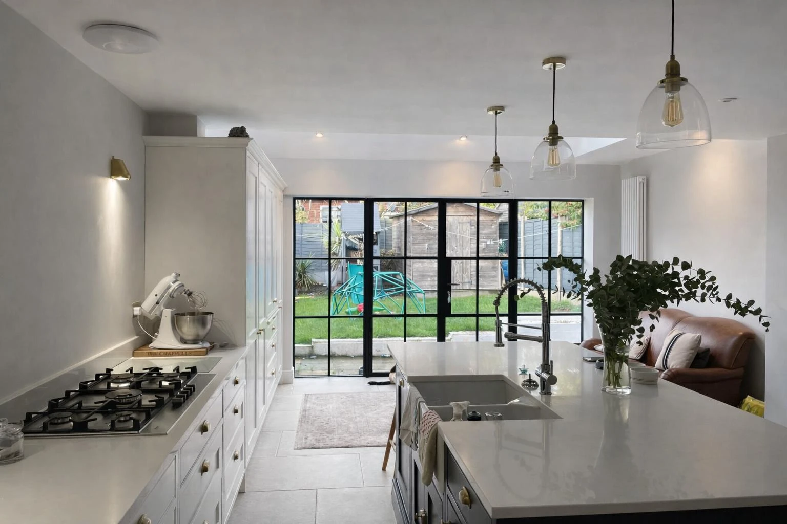 Modern kitchen with a central island, gas stove, and glass doors leading to a garden. Features natural light and stylish decor.