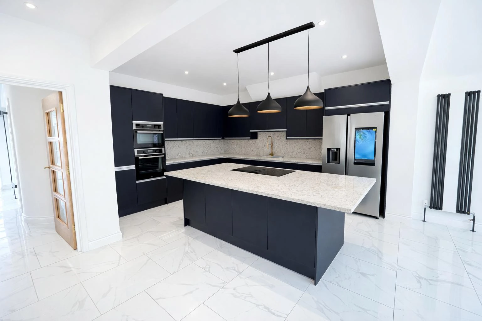 Modern kitchen with dark cabinets, marble countertops, stainless steel appliances, and pendant lighting, featuring white tile flooring.