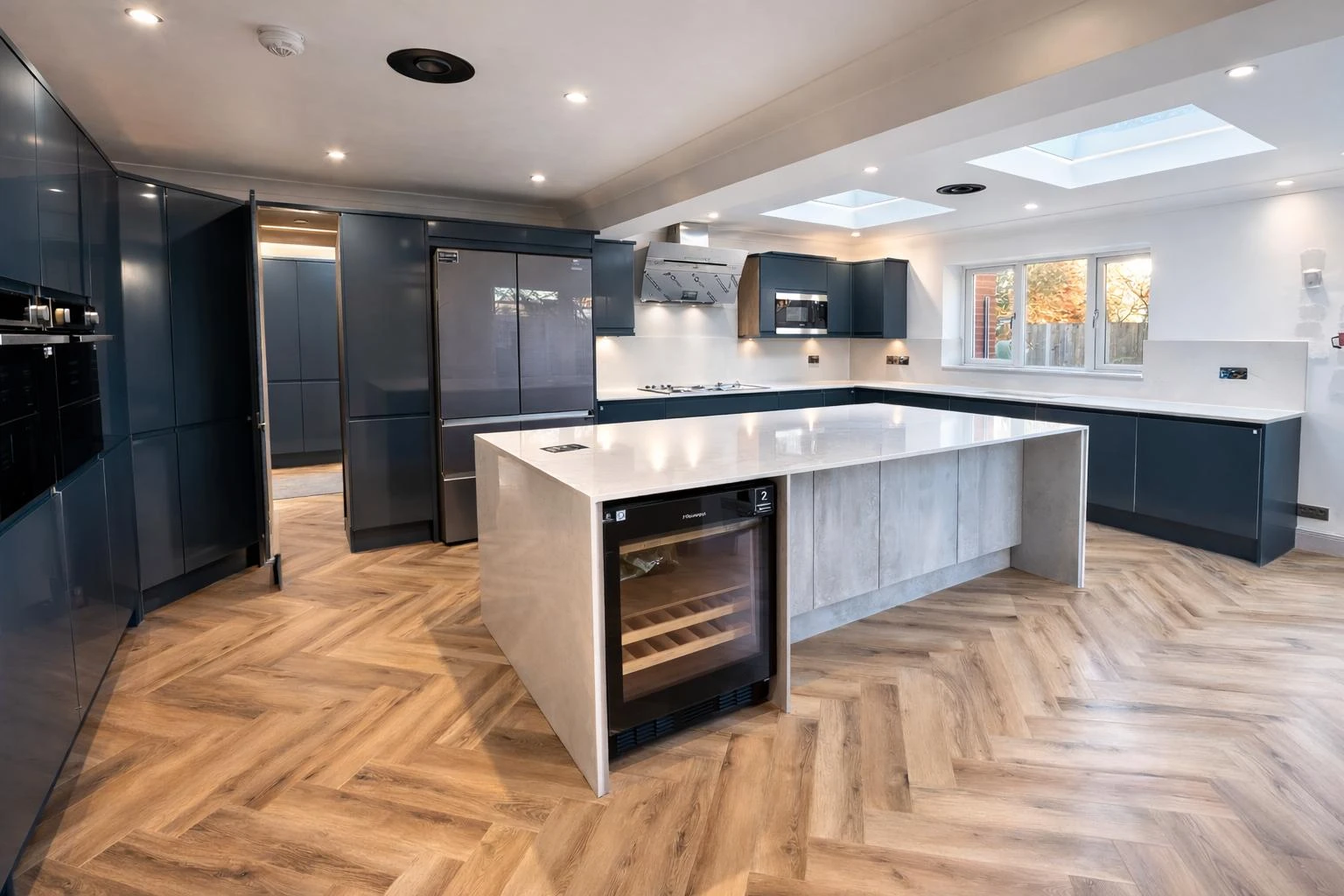 Modern kitchen featuring dark blue cabinets, a central island with a concrete finish, and herringbone patterned wooden flooring.