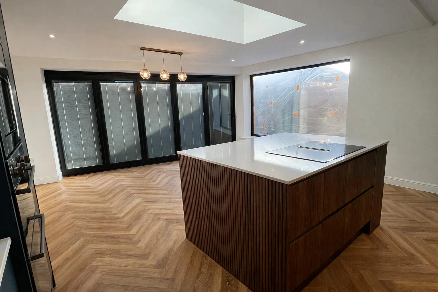 Spacious kitchen featuring a large island, herringbone wooden floor, and windows with sliding doors. Skylight overhead provides natural light.