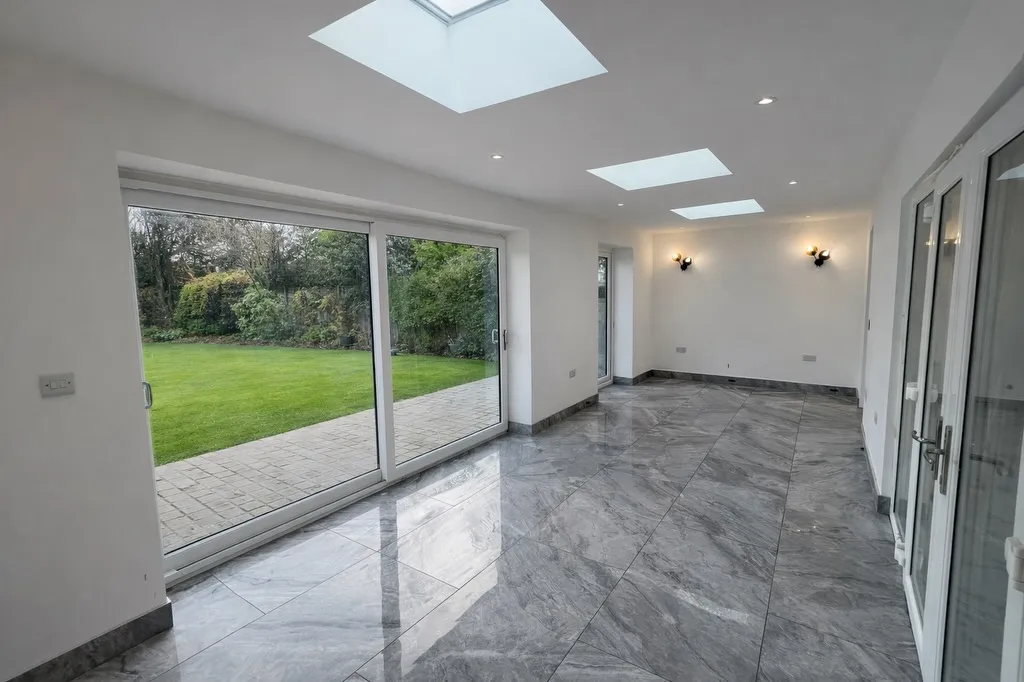 Bright conservatory with marble flooring, large windows, and skylights, overlooking a garden with lush greenery.