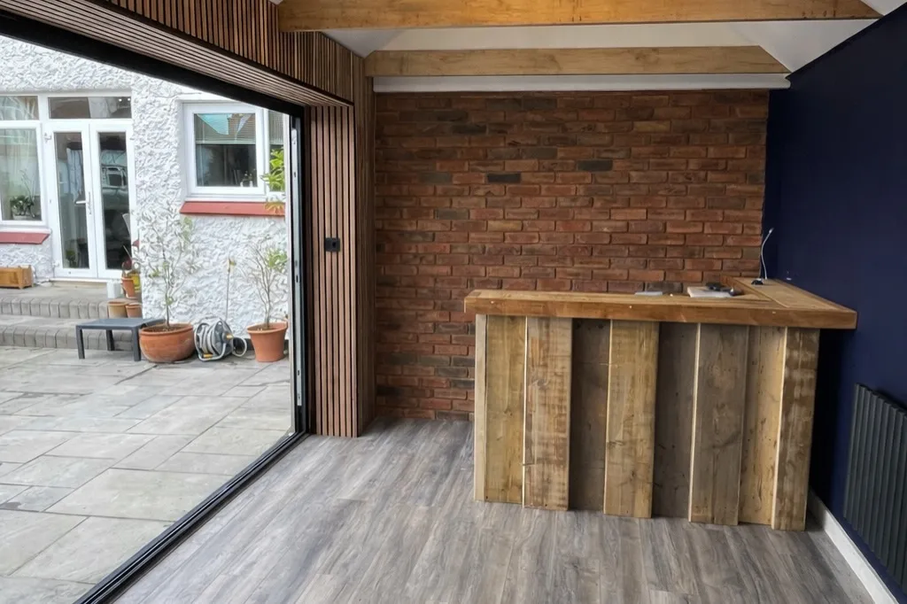 Interior view of a modern space featuring a wooden bar, brick wall, and large glass doors leading to an outdoor area.