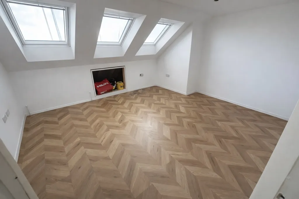 Bright, empty room with herringbone-patterned wood flooring and three skylights on the slanted ceiling. A storage space is visible.
