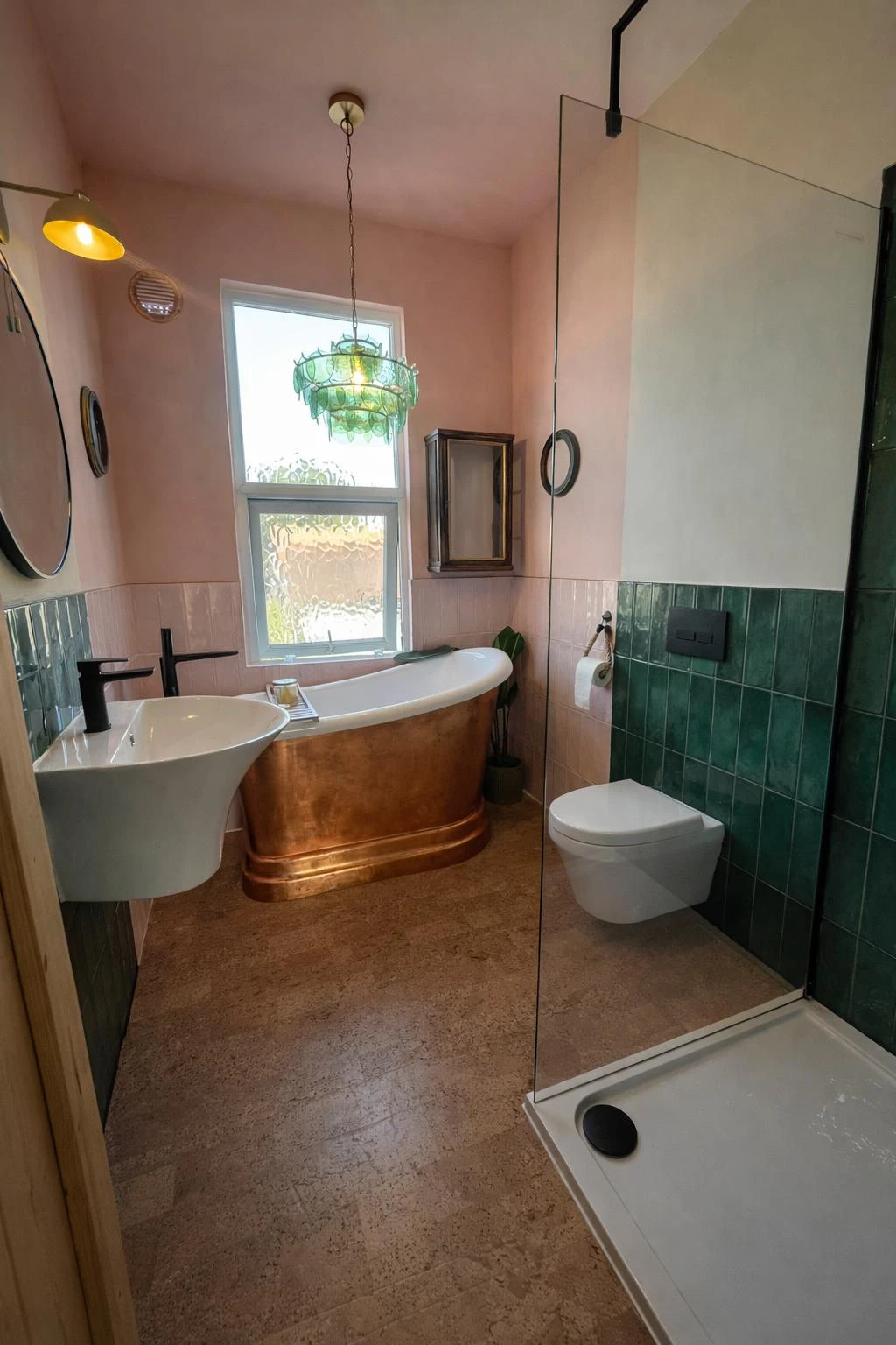 Modern bathroom with a copper bathtub, green tiles, and natural light from a window. Features include a vessel sink and shower area.